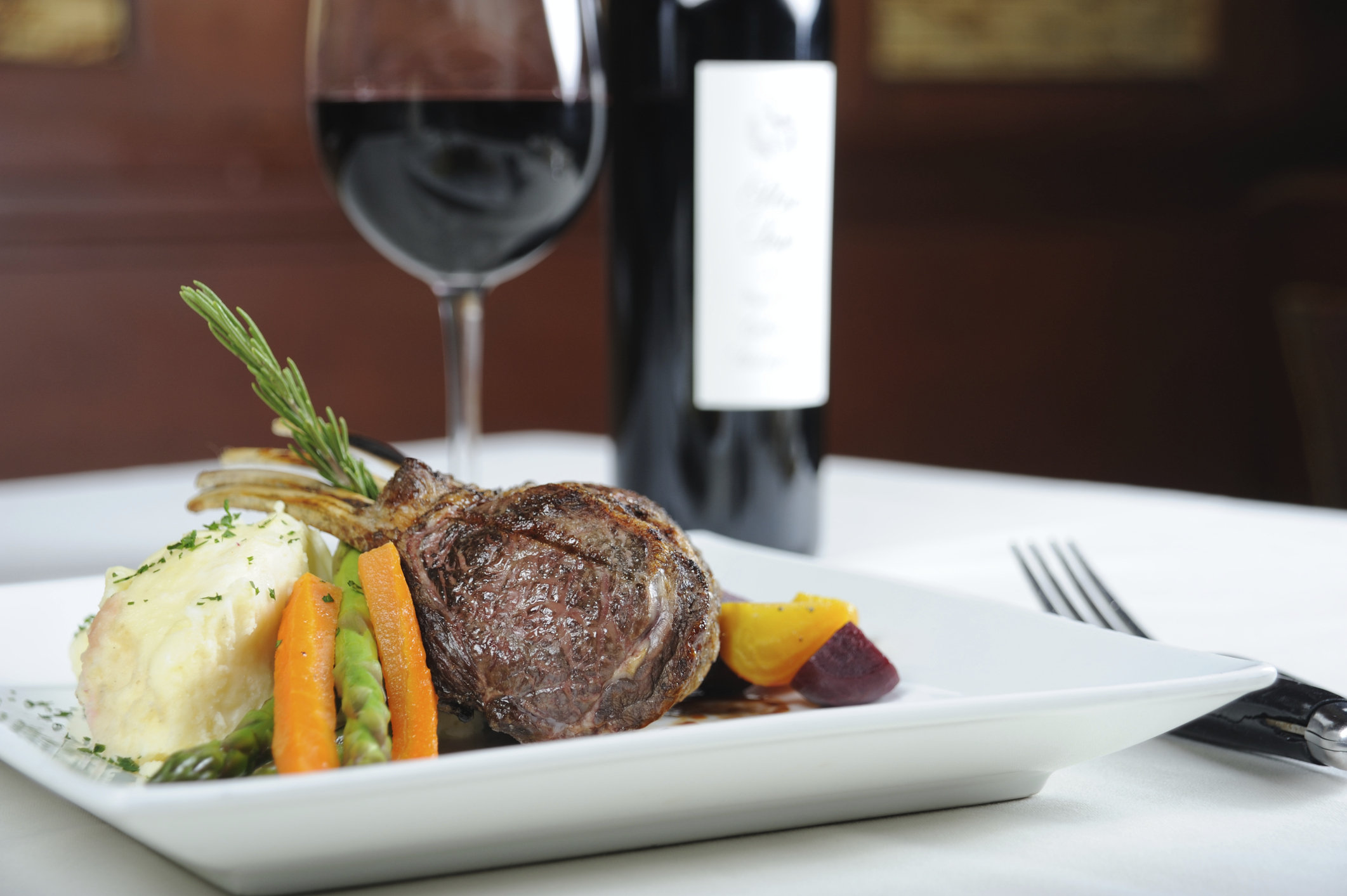 Gourmetgericht mit Fleisch, Gem&uuml;se und Rotwein in elegantem Restaurant