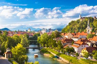 Ljubljana with river, bridge, old town, and castle on hill against mountain backdrop.
