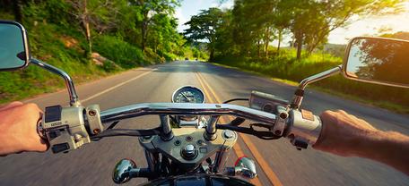 Motorradfahrt auf sonniger Landstraße, Blick über Lenker auf grüne Landschaft.