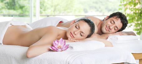 Zwei Personen liegen entspannt auf einem Massagetisch in einem hellen Raum mit Blick ins Grüne.