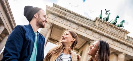 Drei Personen vor dem Brandenburger Tor in Berlin bei Tageslicht.
