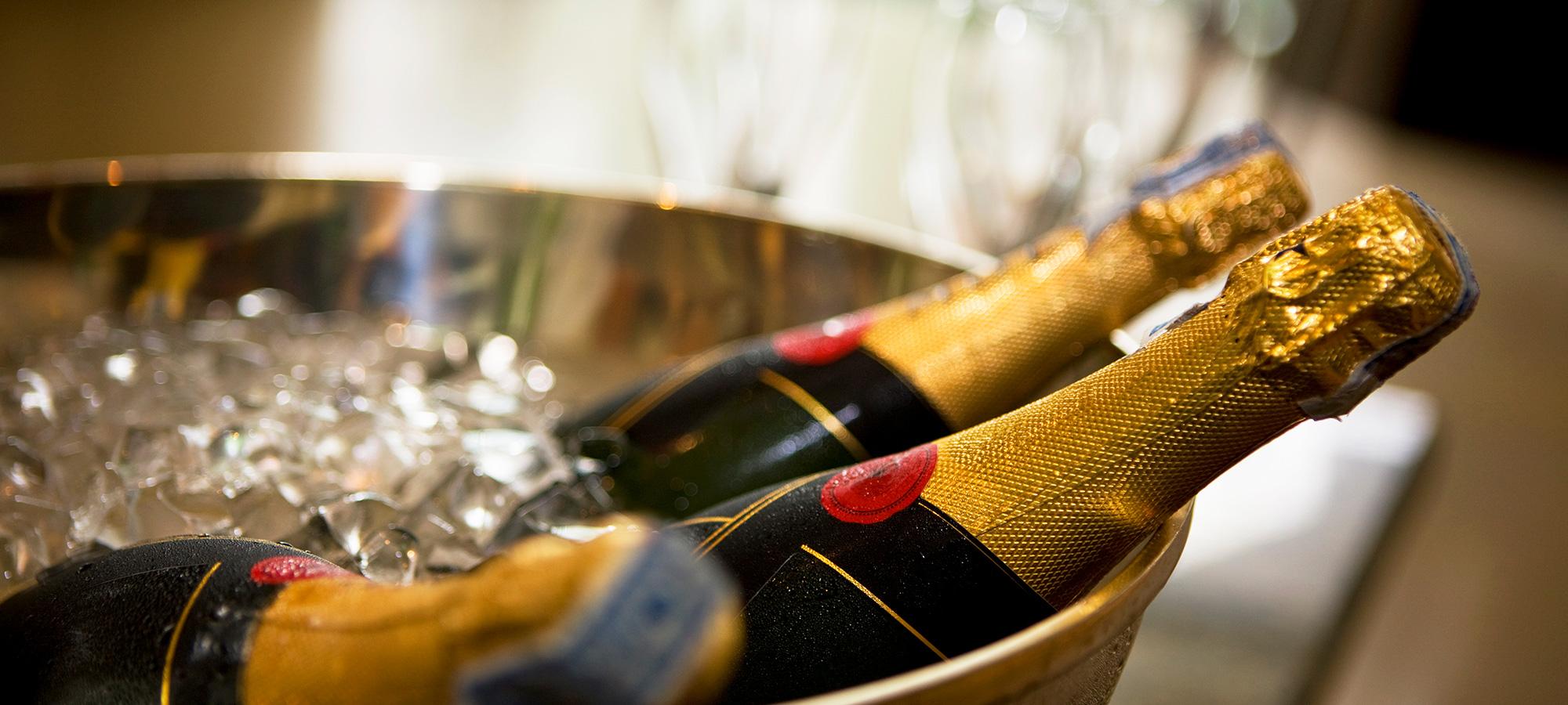 Champagnerflaschen liegen gekühlt auf Eis in einer Metallschale.