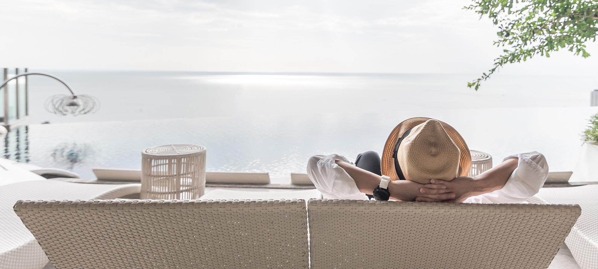 Person entspannt auf Liegen mit Blick auf Infinity‑Pool und ruhiges Meer.