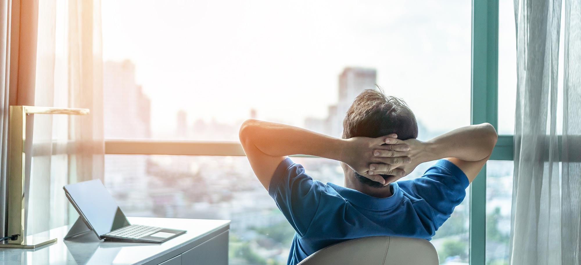Person lehnt sich am Schreibtisch zurück und blickt aus dem Fenster auf die Stadt