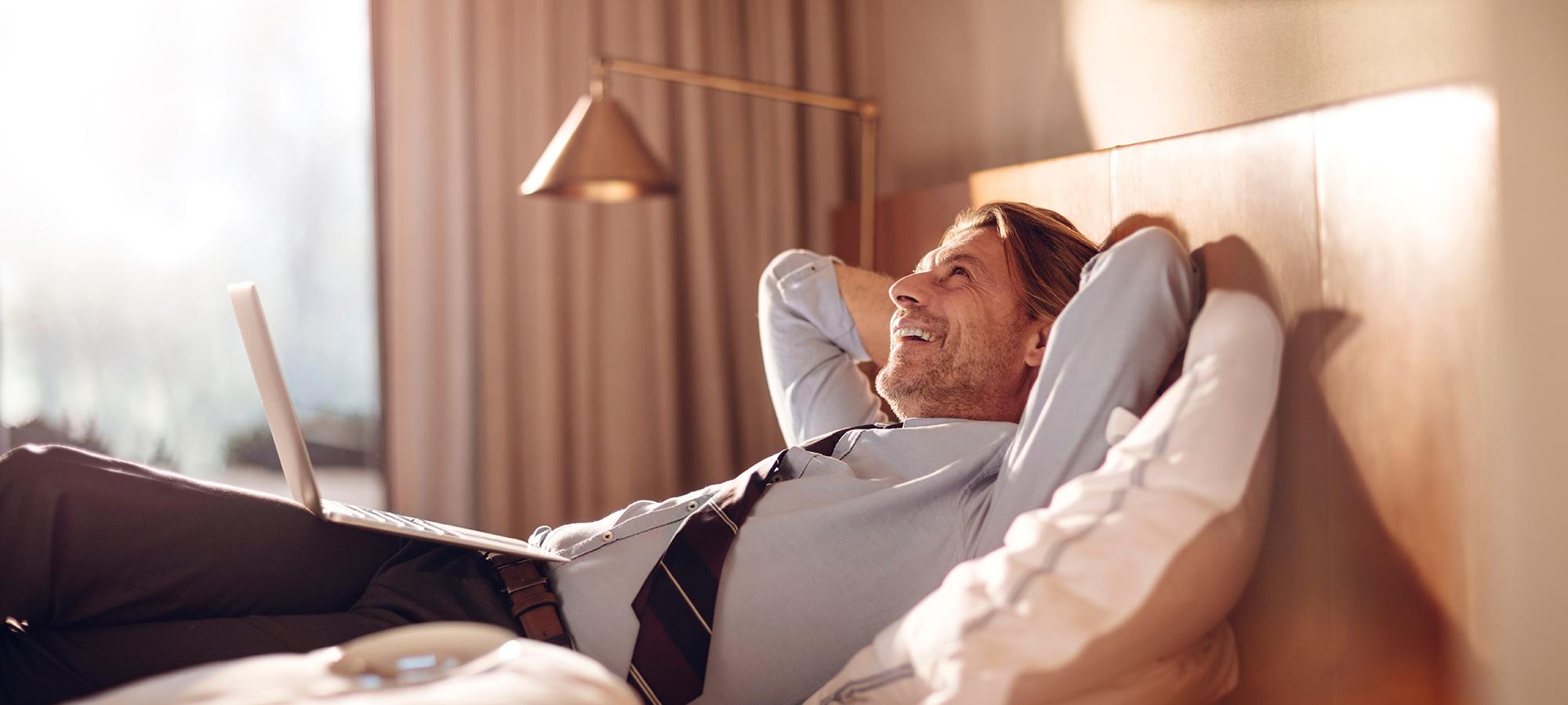 Person entspannt im Hotelzimmer auf dem Bett mit Laptop auf dem Schoß