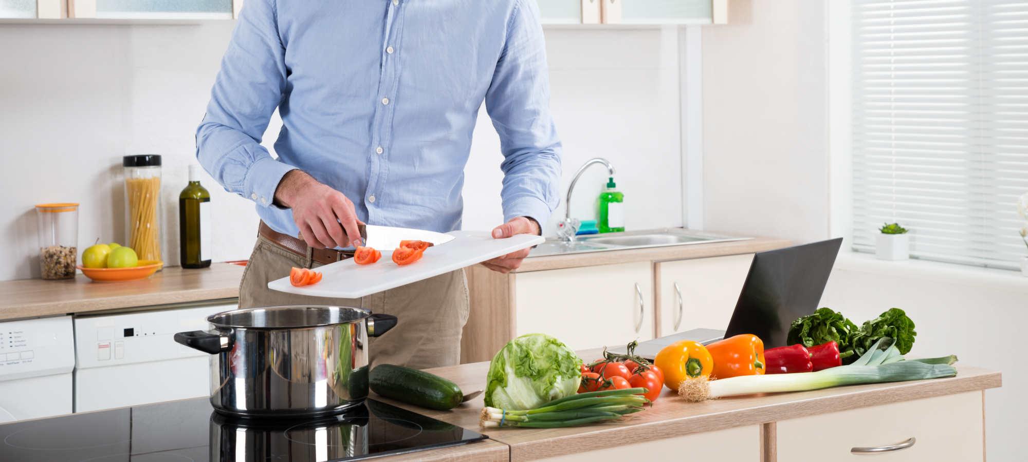 Person kocht Gemüse in moderner Küche mit frischen Zutaten auf der Arbeitsfläche.