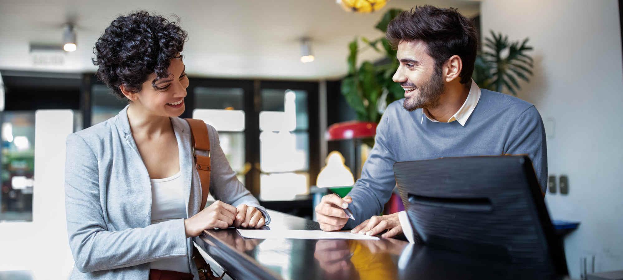 Gast im Hotel an der Rezeption im Gespräch mit Mitarbeitendem