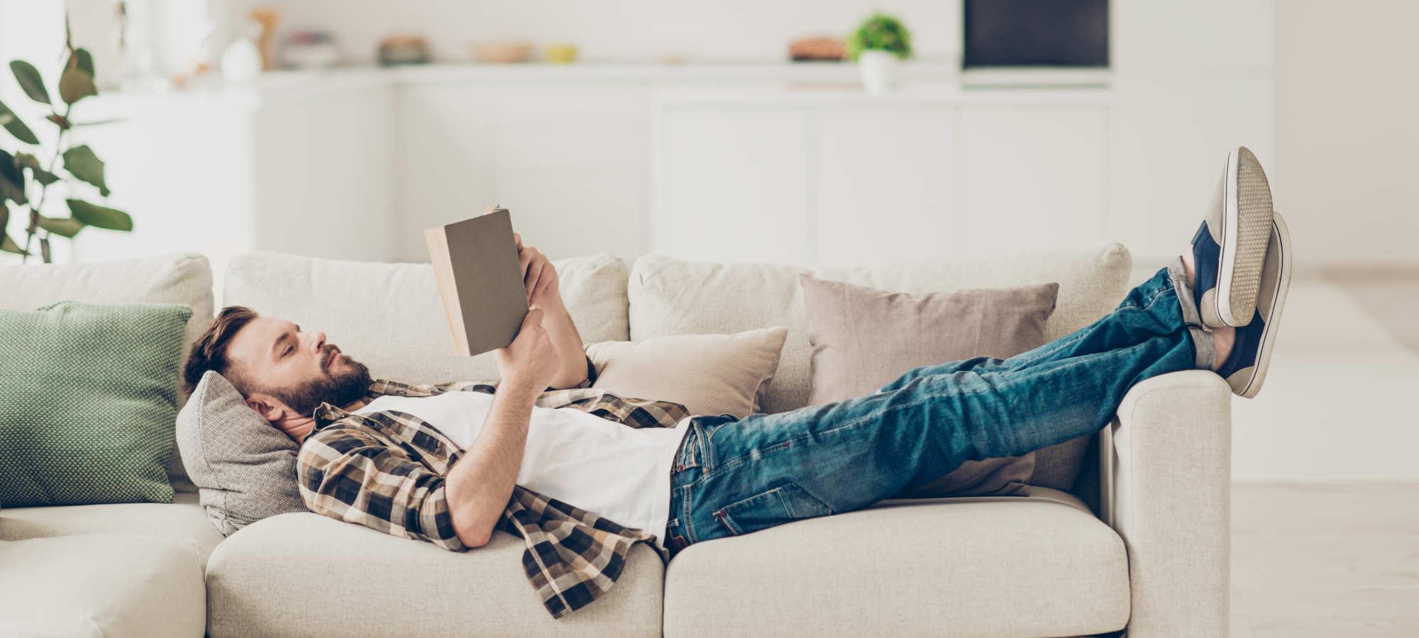 Person liegt entspannt auf dem Sofa und liest ein Buch.