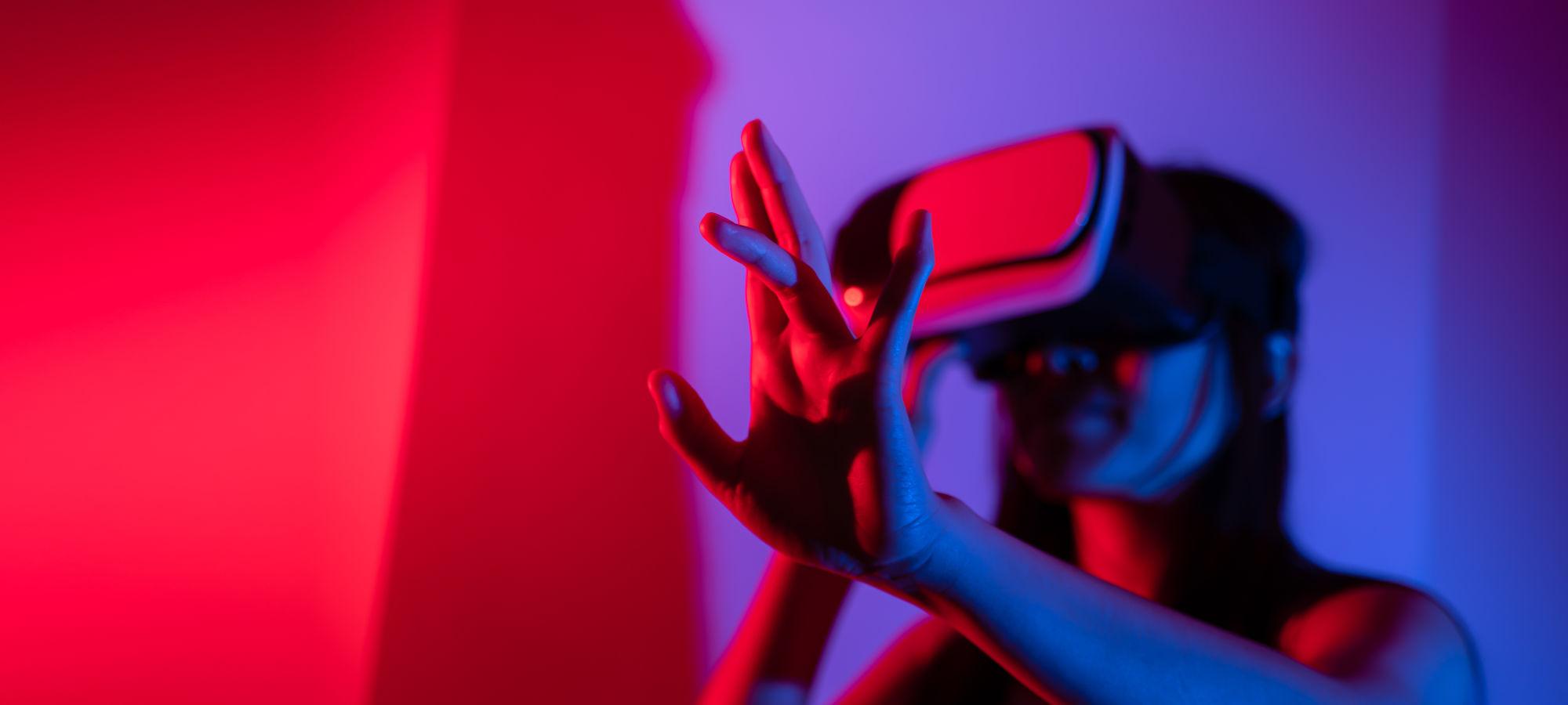 Person mit VR‑Brille in blau‑rotem Licht, Hände nach vorn ausgestreckt.
