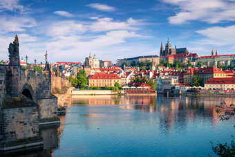 Prague cityscape with colorful buildings by the water and partly cloudy sky.