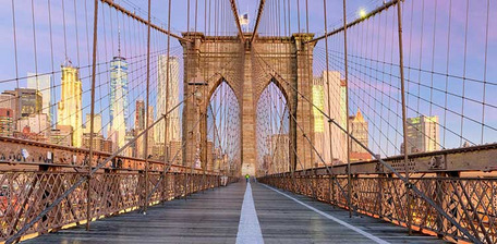 View of Brooklyn Bridge at sunset with NYC skyline in the background.