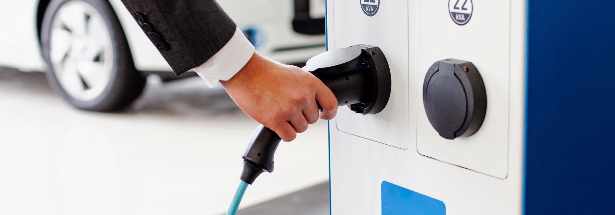 Hand steckt Ladekabel in Elektroauto-Ladestation.