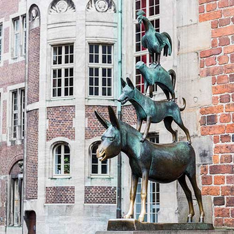 Statue der Bremer Stadtmusikanten vor Backsteingebäude mit Rundbogenfenstern.