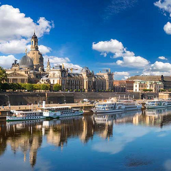 View of Dresden with the Elbe River, boats, and historic old town including Frauenkirche under blue sky.
