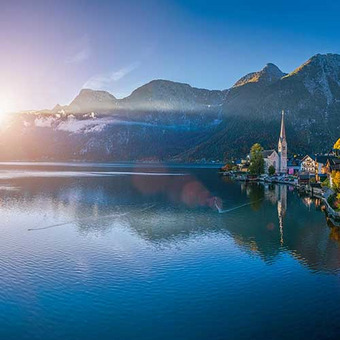 Malerische Seelandschaft mit Bergen und Dorf im Sonnenaufgang. 
