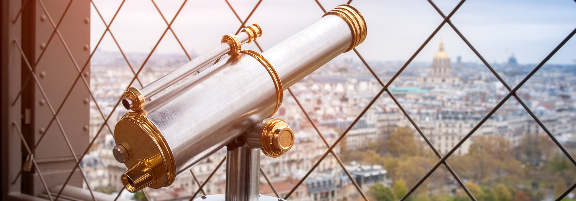 Viewing telescope with gold accents overlooking cityscape and wire fence.