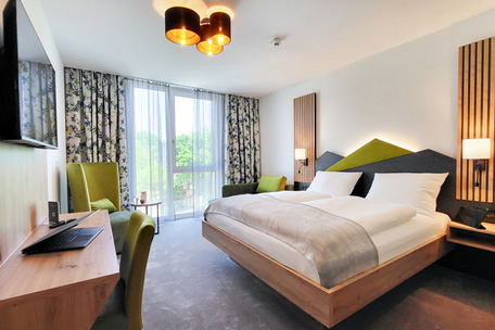 Modern bedroom with large bed, green color accents, bedside tables, desk, chair and large windows with curtains.