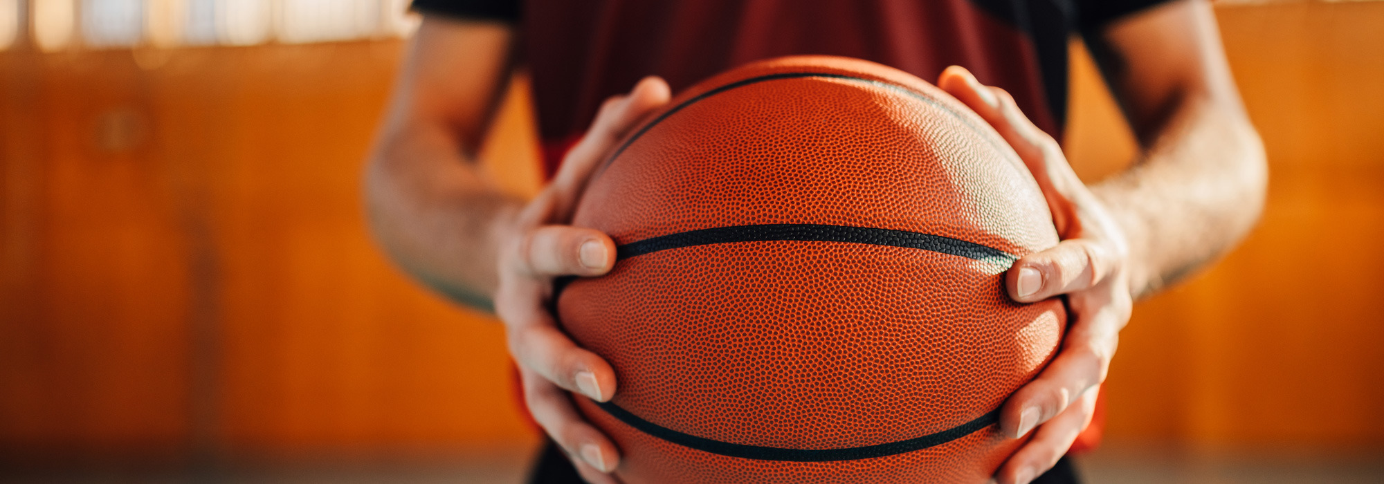 Close-up of a person holding a basketball with both hands inside a gym.