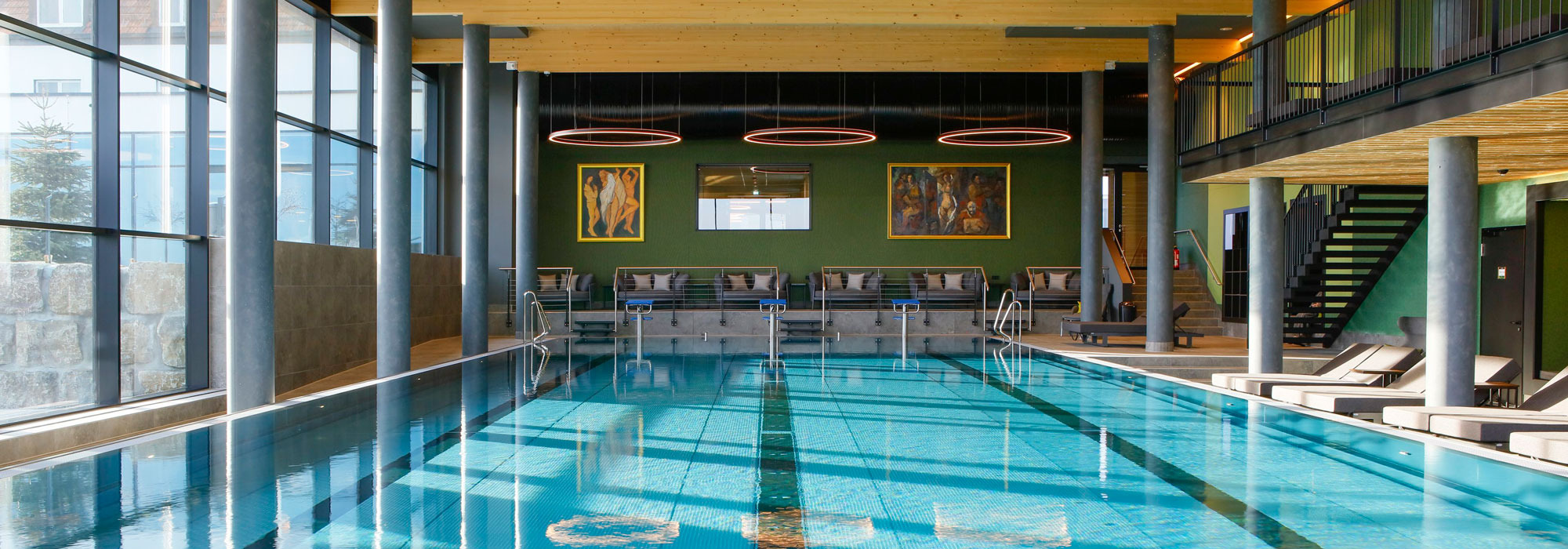 Moderner Innenpool mit Liegen, Holzdecke und großen Fenstern in stilvoller Umgebung.