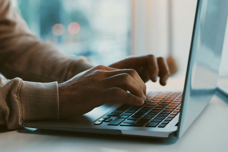 Hände tippen auf Laptop-Tastatur, unscharfer Hintergrund mit natürlichem Licht.