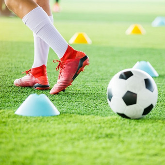 Fußballtraining auf Rasen mit Ball, roten Schuhen und bunten Markierungshütchen.