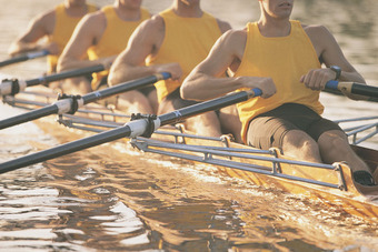 Rowing team in yellow jerseys rows in sync on sunlit water.