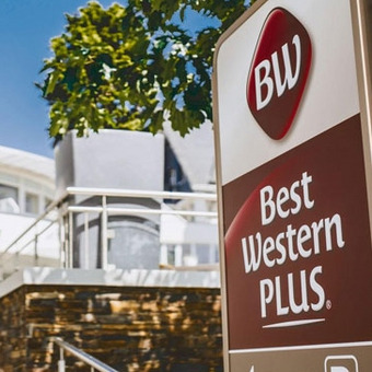 Exterior view of the modern Best Western Plus Hotel in Willingen with logo, large windows, and greenery under a clear sky.