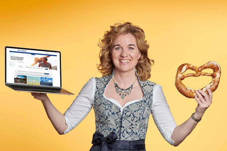 Gundi Mitzel with laptop and pretzel in front of yellow background – a passionate host.
