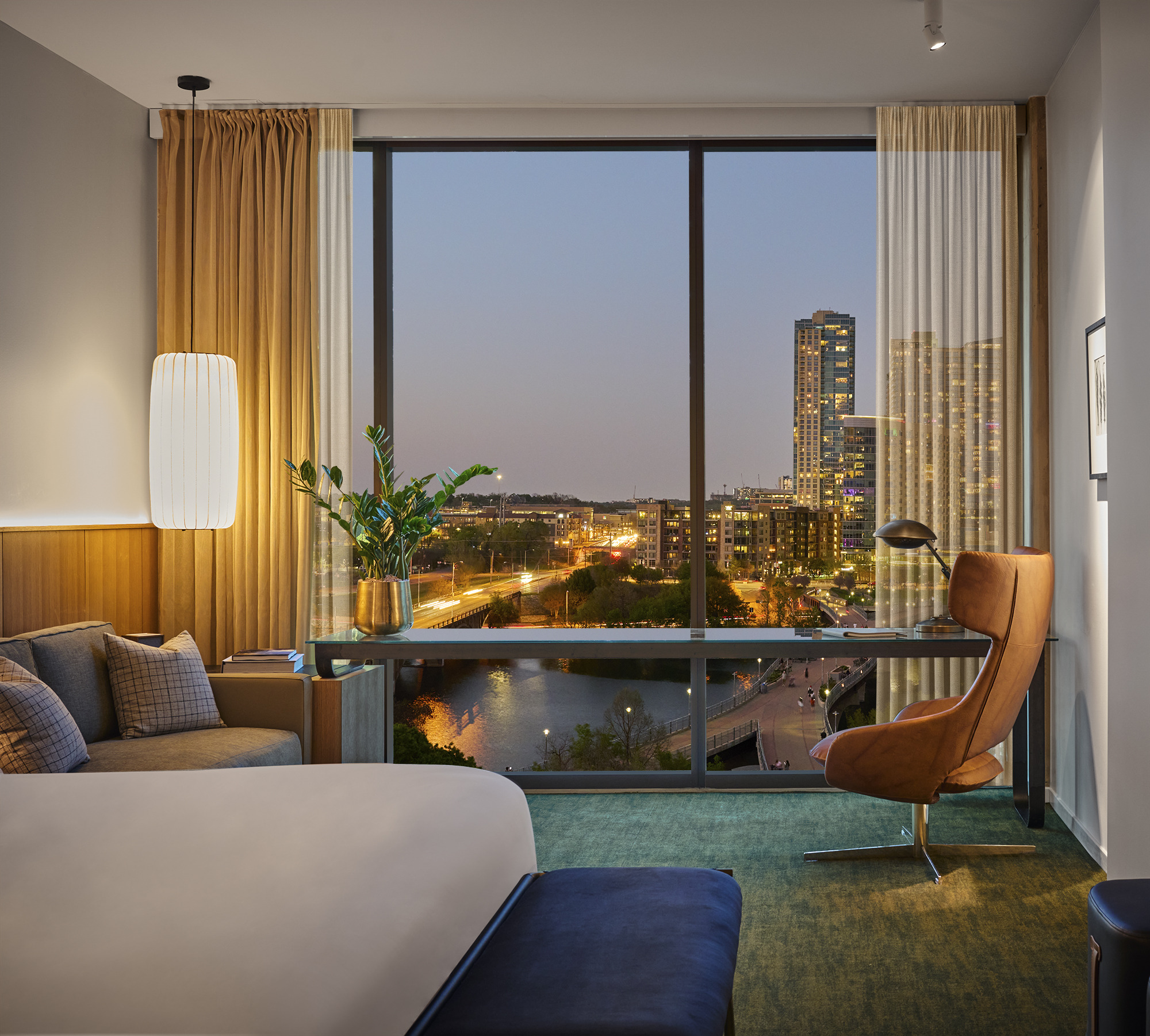 Modernes Hotelzimmer mit Sessel, großer Fensterfront und nächtlichem Stadtblick.