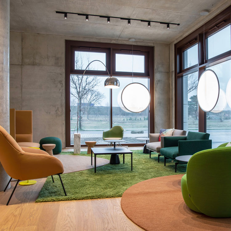 Moderner Lounge-Bereich mit gro&szlig;en Fenstern, gr&uuml;nen Sesseln und stilvollen Lampen.