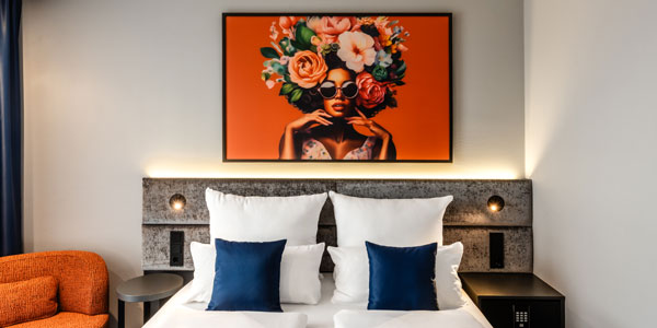 Modernes Hotelzimmer mit Doppelbett, wei&szlig;en Kissen und Kunstwerk mit Blumenmotiv.