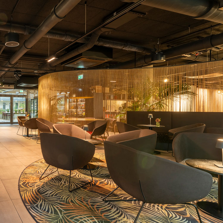 Stilvolle Hotellounge mit modernen Sesseln, goldener Raumtrennung und Pflanzen.