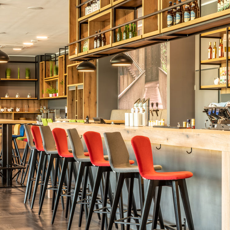 Moderne Hotelbar mit hohen Holzregalen, bunten Barhockern und Flaschen-Dekor.