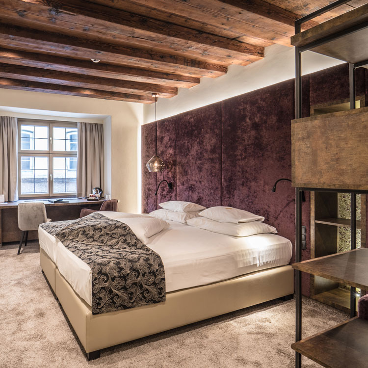 Hotelzimmer mit Doppelbett, Holzbalkendecke und Schreibtisch am Fenster.