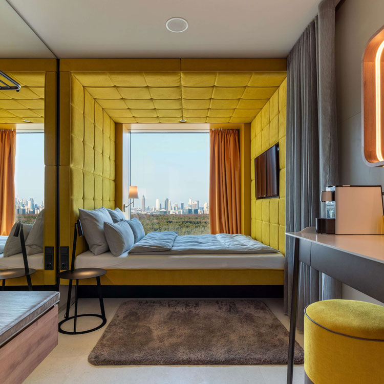 Kompaktes Hotelzimmer mit gelber Polsterung und Blick auf die Skyline.