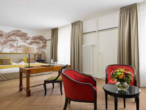 Elegantes Hotelzimmer mit Holzboden, Schreibtisch und roten Sesseln.