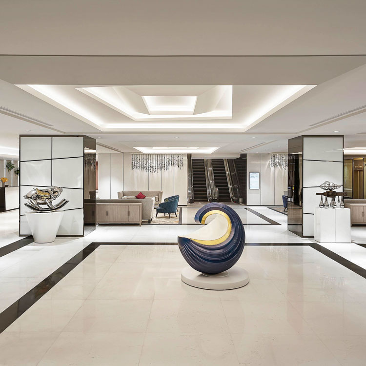 Moderne Hotellobby mit Skulptur und Sitzbereich vor Rolltreppen.