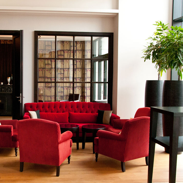 Sitzbereich mit roten Sesseln und Sofa vor einer Glaswand mit B&uuml;cherdekor.