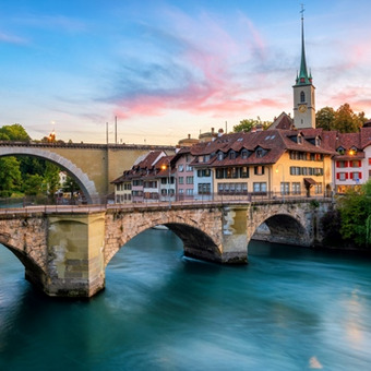 Bern mit historischem Brückenbogen, Altstadt und Kirchturm bei Sonnenuntergang.