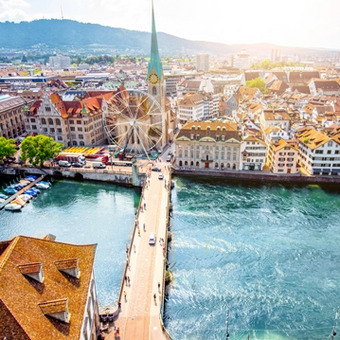 Zurich with Limmat River, historic buildings, green hills and sunshine.