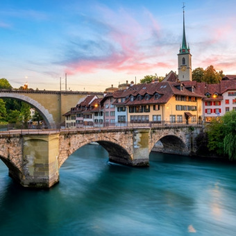 Bern with historic arched bridge, old town, and church steeple at sunset.