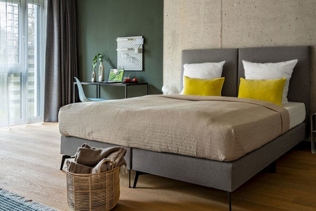 Modern bedroom with double bed, concrete wall, desk, and large windows.