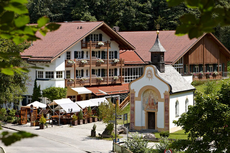 Alpenhaus mit Balkonen, Kapelle und Caféterrasse in grüner Landschaft