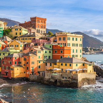 Bunte Küstenhäuser an einer Felsbucht mit Meerblick und Bergen im Hintergrund.