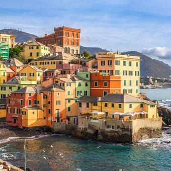 Colorful seaside houses along a rocky bay with sea view and mountains behind.
