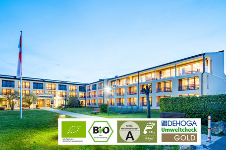 Modernes Hotel bei Abenddämmerung mit Umwelt- und Bio-Zertifikaten im Vordergrund.