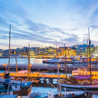 Beleuchteter Hafen mit Booten vor moderner Stadtkulisse in der Abenddämmerung.