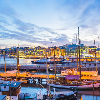 Illuminated harbor with boats and modern cityscape at dusk.
