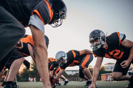 American-Football-Spieler in Startposition, Trikots in Schwarz-Orange, Nummer 20 im Vordergrund.