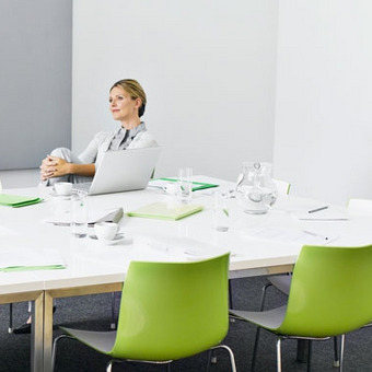 Modern conference room with white table, green chairs and a laptop on the table.